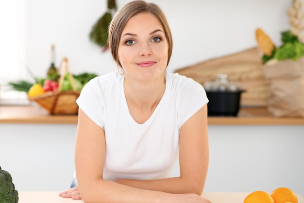 Junge Frau ist bereit zum Kochen in einer Küche Hausfrau sitzt am Tisch und schaut in die Kamera