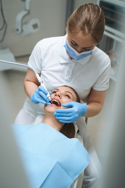 Junge Frau ist im Zahnarztstuhl, während sie ihren Zahn von einem Spezialisten in einer modernen Klinik bohrt