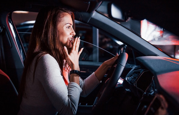 Junge Frau ist in einem brandneuen modernen Automobil mit roter Beleuchtung.