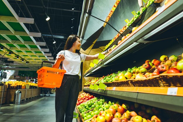 Junge Frau kauft im Supermarkt ein und wählt Äpfel im Laden aus