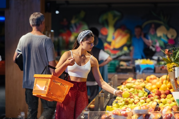 Junge Frau kauft im Supermarkt ein und wählt Äpfel im Laden aus