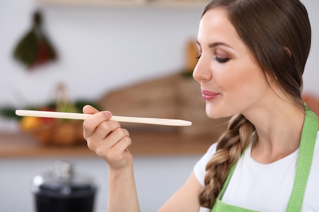 Junge Frau kocht in einer Küche Hausfrau probiert die Suppe mit einem Holzlöffel