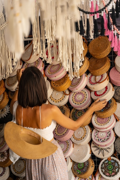 Junge Frau kommt in einen lokalen Korbwarenladen, um während ihrer Reise exotische Taschen zu kaufen