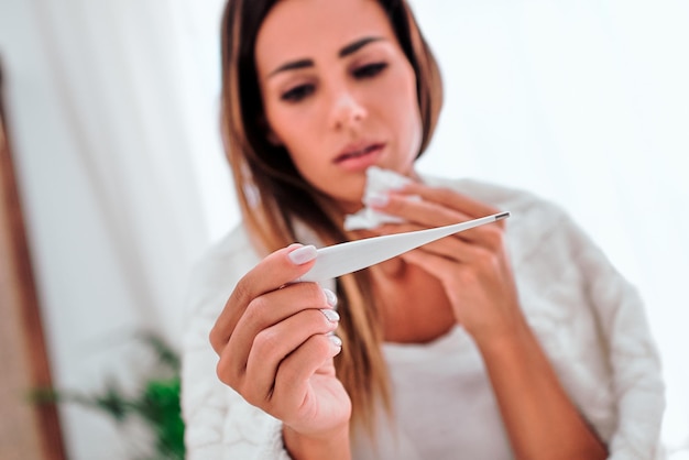 Junge Frau krank im Bett mit hoher Temperatur Fokus auf Thermometer Nahaufnahme