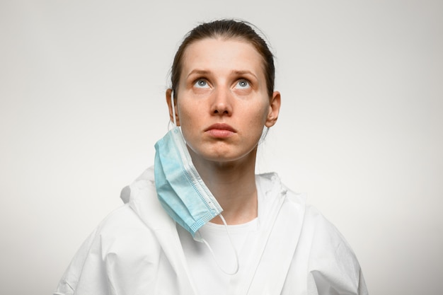 Junge Frau Krankenschwester, die mit entfernter medizinischer Maske steht und aufschaut