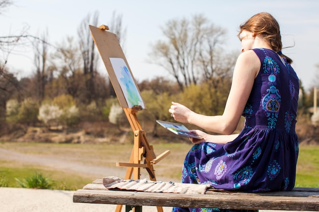 Junge Frau kreativer Maler zeichnet Pinsel Aquarellfarben auf Leinwand im Freien Frühlingsinspiration Künstlerin malt Landschaft