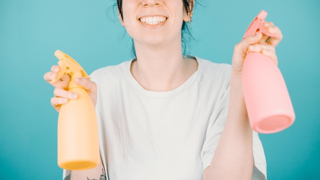 Junge Frau lächelt glücklich in die Kamera, während sie ein Paar Wassersprüher hält, um sich im Sommer zu erfrischen Farbhintergrundbild