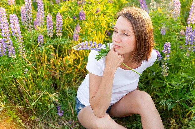 Junge Frau lächelt im Freien schönes Brunete-Mädchen, das auf Sommerfeld mit blühenden wilden Blumen ruht