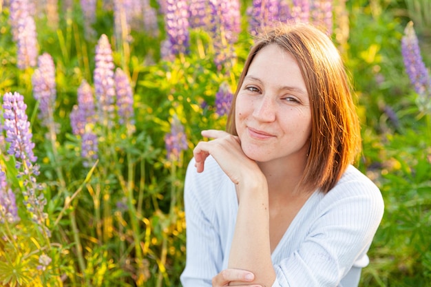 Junge Frau lächelt im Freien schönes Brunete-Mädchen, das auf Sommerfeld mit blühenden wilden Blumen ruht