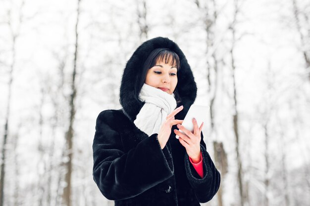 Junge Frau lächelt mit Smartphone und Winterlandschaft