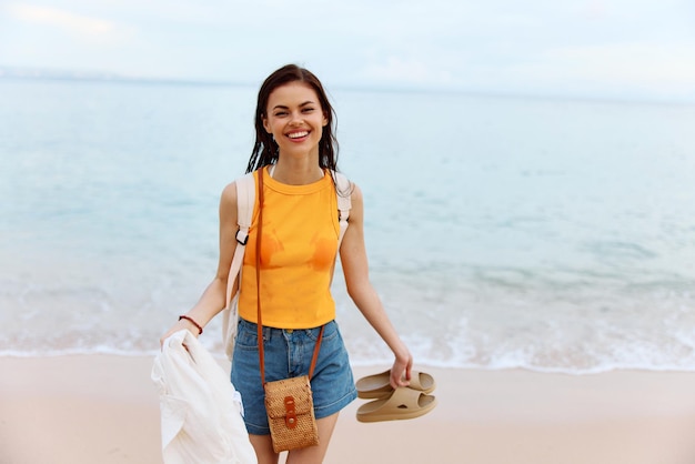 Junge Frau lächelt mit Zähnen, nachdem sie mit einem Rucksack in nasser Kleidung im Meer geschwommen ist und im Sommerurlaub auf der Insel am Meer bei Bali-Sonnenuntergang am Strand entlang spaziert