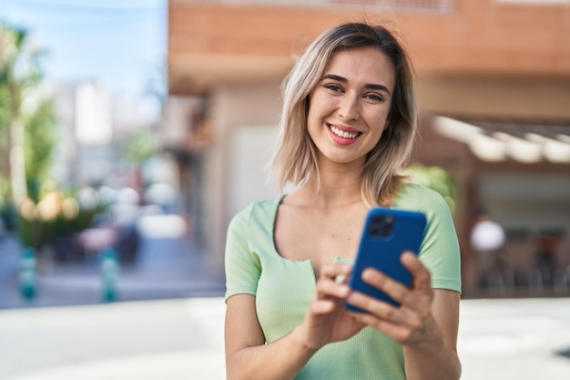 Junge Frau lächelt selbstbewusst mit Smartphone auf der Straße
