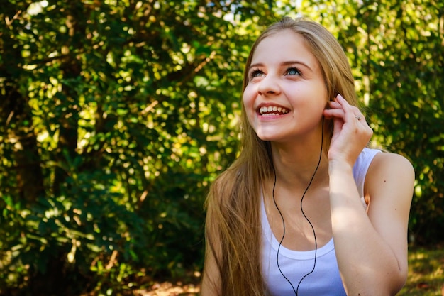 Junge Frau lächelt, während sie im Park Musik hört