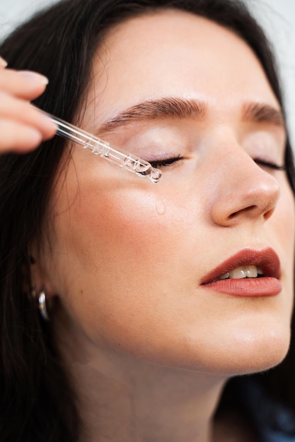 Foto junge frau legt ein feuchtigkeitsserum auf das gesicht auf, mädchen mit hyaluronsäure oder serumpipette in den händen, nahaufnahme