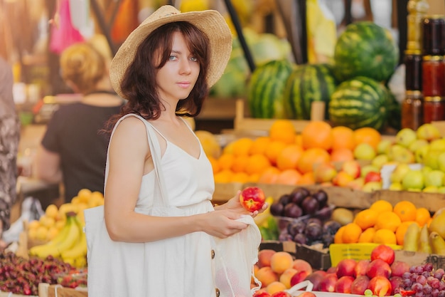 Junge Frau legt Obst und Gemüse in Baumwollbeutel auf dem Lebensmittelmarkt. Wiederverwendbare Öko-Tasche zum Einkaufen. Zero-Waste-Konzept.