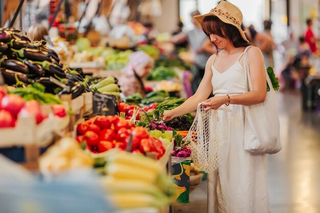 Junge Frau legt Obst und Gemüse in Baumwollbeutel auf dem Lebensmittelmarkt. Wiederverwendbare Öko-Tasche zum Einkaufen. Zero-Waste-Konzept.