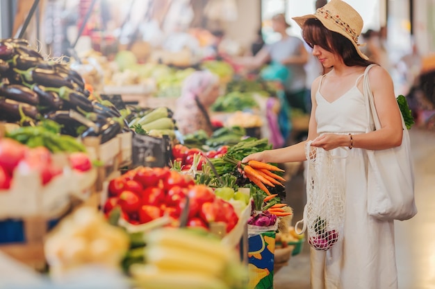 Junge Frau legt Obst und Gemüse in Baumwollbeutel auf dem Lebensmittelmarkt. Wiederverwendbare Öko-Tasche zum Einkaufen. Zero-Waste-Konzept.