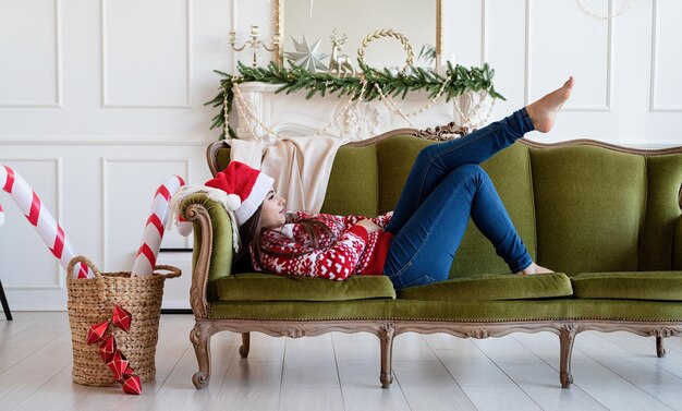 Junge Frau liegt allein auf der Couch in einem weihnachtlich dekorierten Wohnzimmer
