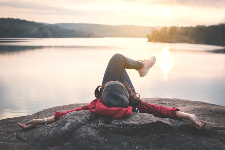 Foto junge frau liegt auf einem felsen am see vor klarem himmel