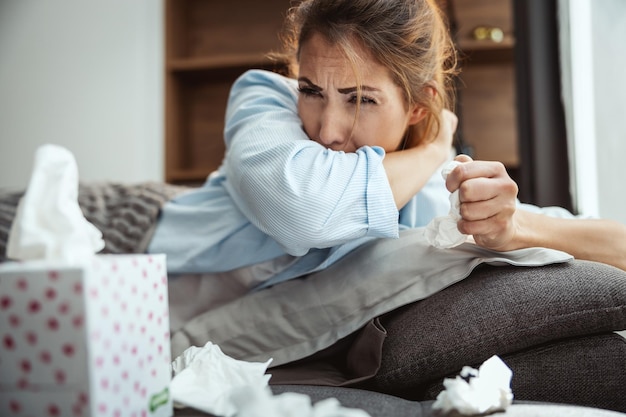 Junge Frau liegt krank zu Hause auf der Couch und hustet.