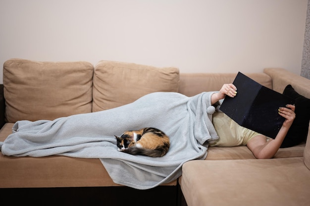 Junge Frau liegt zu Hause im Bett und liest mit ihrer Katze ein Buch