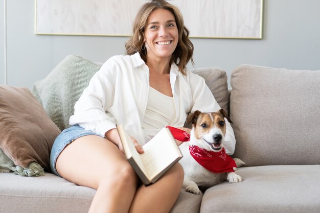 Junge Frau liest Buch und ihren süßen Hund auf dem Sofa zu Hause. Schönes Haustier.