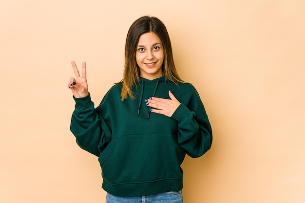 Junge Frau lokalisiert auf Beige, die einen Eid leistet und Hand auf Brust legt.