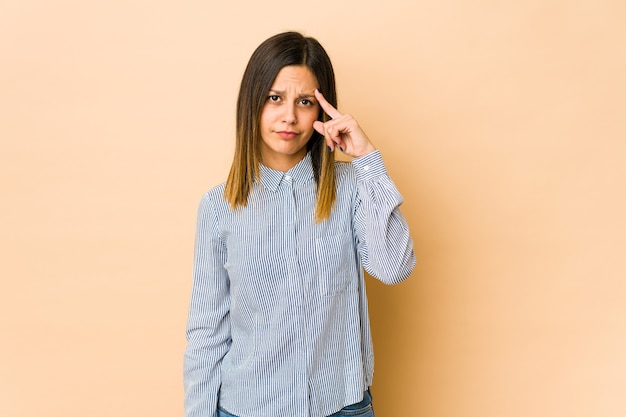 Junge Frau lokalisiert auf beige Wand, die Tempel mit Finger zeigt, denkend, konzentrierte sich auf eine Aufgabe.