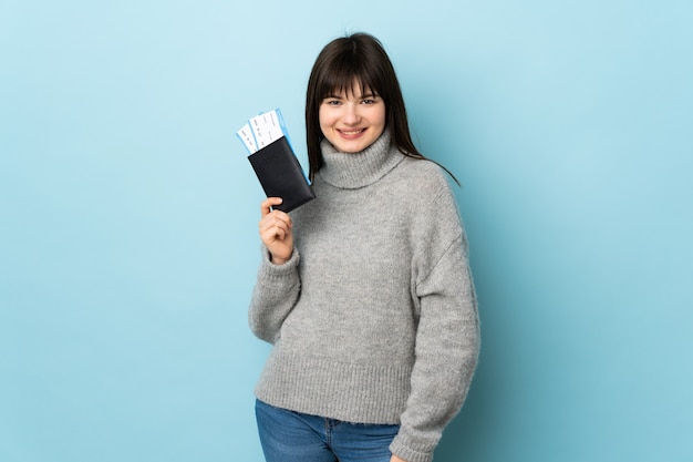 Junge Frau lokalisiert auf blau glücklich im Urlaub mit Pass und Flugtickets