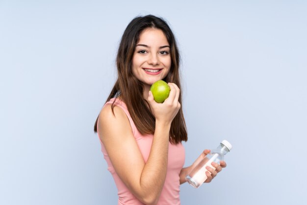 Junge Frau lokalisiert auf Blau mit einem Apfel und mit einer Flasche Wasser