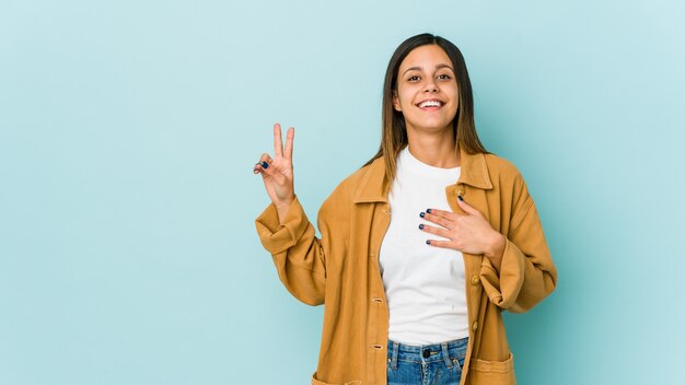 Junge Frau lokalisiert auf blauer Wand, die einen Eid leistet und Hand auf Brust legt.