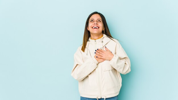 Junge Frau lokalisiert auf der blauen Wand, die lachend Hände auf Herz hält, Konzept des Glücks.