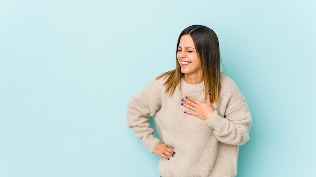 Junge Frau lokalisiert auf der blauen Wand, die lachend Hände auf Herz hält, Konzept des Glücks.