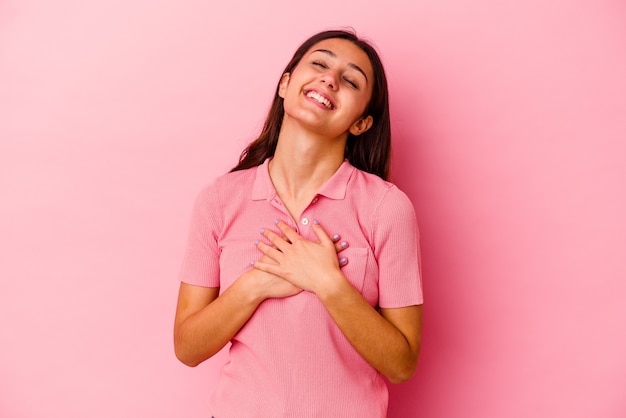 Junge Frau lokalisiert auf rosa Wand, die lachend Hände auf Herz hält