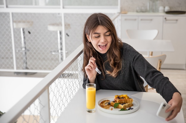 Junge Frau macht ein Selfie beim Frühstück, belgische Waffeln und Saft zum Frühstück.