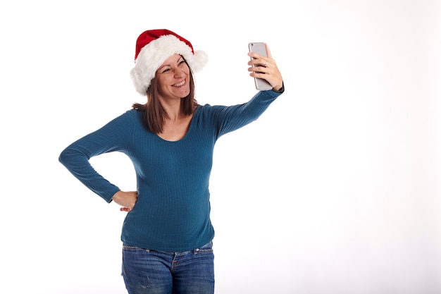 Junge Frau macht ein Selfie mit ihrem Handy und trägt eine Weihnachtsmütze