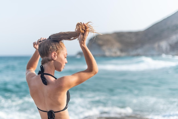 Junge Frau macht einen Pferdeschwanz am Strand mit dem Rücken zum horizontalen Bild der Kamera