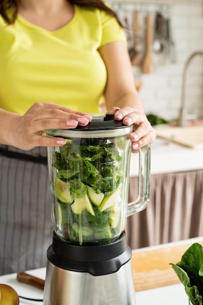 Junge Frau macht grünen Spinat-Smoothie in der heimischen Küche