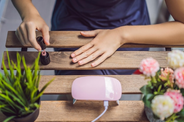 Junge Frau macht Maniküre mit Gelpolitur und UV-Lampe in rosa Farbtönen