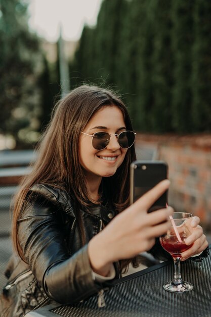 Junge Frau macht Selbstporträt mit Smartphone. Mädchen, das selfie macht. Frau im Café. Frau allein. Selbstporträt im Café im Freien. lächeln. lächelnd. Gerät. Selbstportrait. Kaffeepause. Kaffeezeit