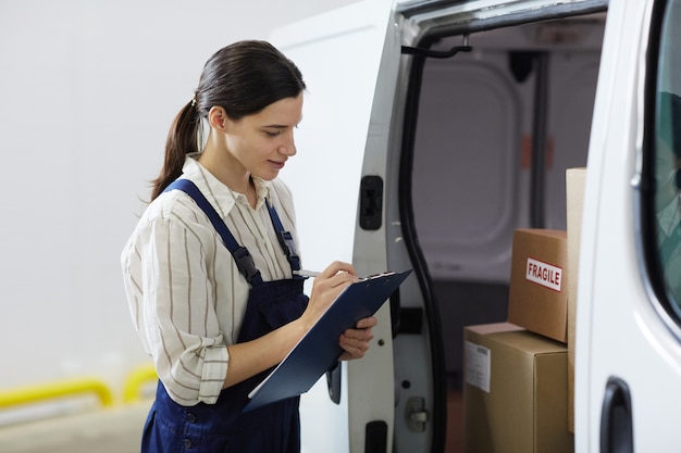 Junge Frau macht sich Notizen in der Zwischenablage und registriert die Kisten im LKW vor der Lieferung