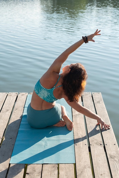 Junge Frau macht Yoga auf dem Pier in der Nähe des Flusses