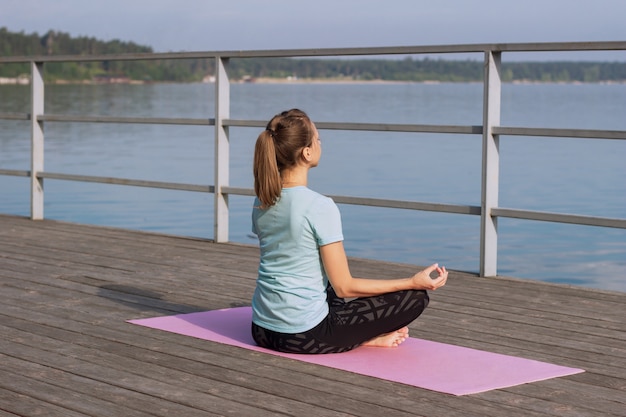 Junge Frau macht Yoga auf einer rosa Matte auf einem Pier am Meer