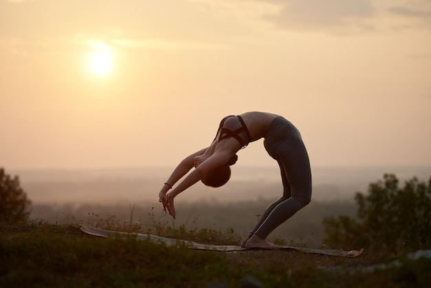 Junge Frau macht Yoga-Übungen im Freien bei Sonnenuntergang
