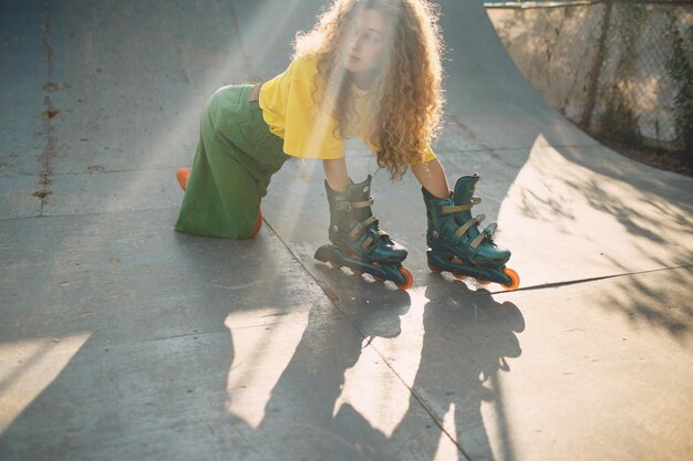 Junge Frau Mädchen in grüner und gelber Kleidung und orangefarbenen Strümpfen mit lockiger Frisur mit Rollen an der Hand Rollschuhläuferin im Skatepark