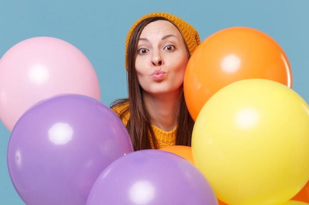 Junge Frau Mädchen in Pullover Hut posiert isoliert auf blauem Hintergrund. Geburtstagsfeier, Menschen-Emotion-Konzept. Mock-up-Kopienbereich. Feiern halten bunte Luftballons, die Luftküsse senden.