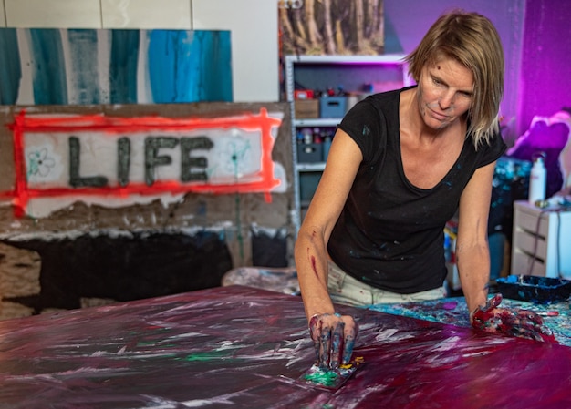 Junge Frau malt ein abstraktes Gemälde mit ihren Händen in ihrem Innenstudio,