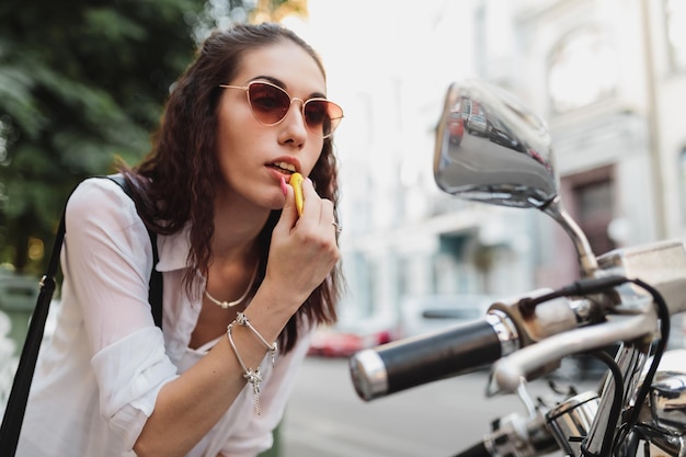 Junge Frau malt ihre Lippen und schaut in den Spiegel eines hochwertigen Motorradfotos