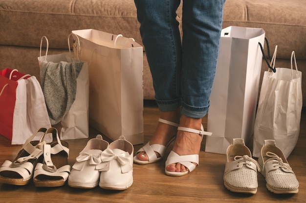 Junge Frau messen neue Schuhe und stehen zwischen Einkaufstaschen zu Hause, Lieferung und Einkaufskonzept