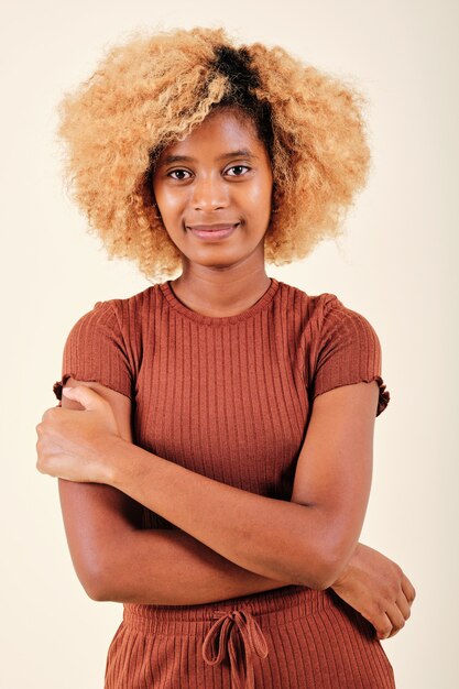 Junge Frau mit Afro-Frisur, die in die Kamera schaut und lächelt, während sie über einem isolierten Hintergrund posiert.